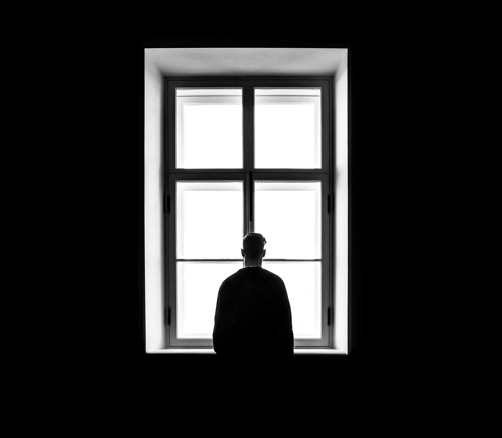 Black and white photo of person standing in front of a window with their back to the camera